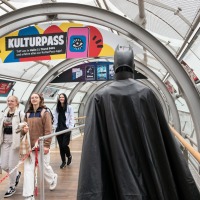 Eine als Batman verkleidete Person läuft über die Manga-Comic-Con, andere Besucher:innen schauen interessiert Eine als Batman verkleidete Person läuft über die Manga-Comic-Con, andere Besucher:innen schauen interessiert