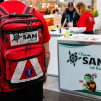 eine Personen vom Awareness Team SAM der Manga Comic Con 2025 läuft am Stand vorbei, dabei sieht man deutlich den roten Rucksack des Teams eine Personen vom Awareness Team SAM der Manga Comic Con 2025 läuft am Stand vorbei, dabei sieht man deutlich den roten Rucksack des Teams