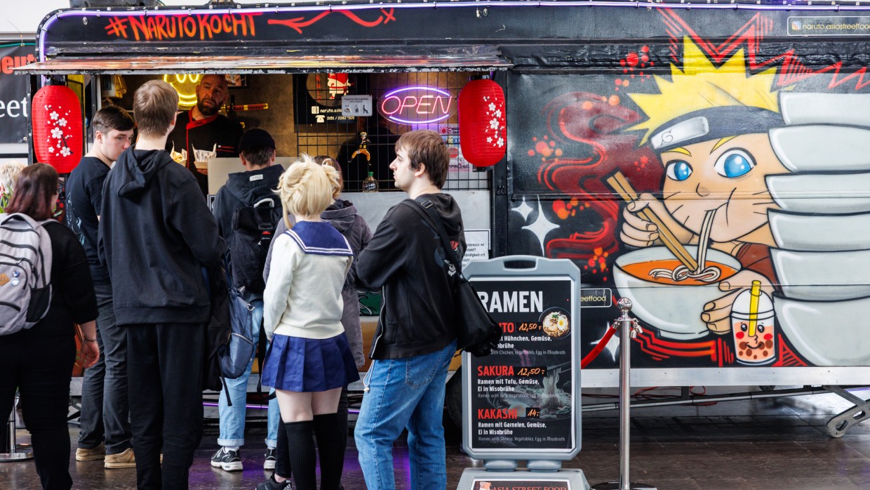 Mehrere Personen stehen vor einem Food Truck in der Schlange auf der Manga Comic Con 2025. Der Food Truck ist beschriftet mit "Naruto kocht" und trägt eine Zeichnung von einer Nudeln-essenden Mangafigur. Mehrere Personen stehen vor einem Food Truck in der Schlange auf der Manga Comic Con 2025. Der Food Truck ist beschriftet mit "Naruto kocht" und trägt eine Zeichnung von einer Nudeln-essenden Mangafigur.