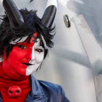 Person mit rot-weiß geschminktem Gesicht, schwarzen Hörnern und Cosplay-Outfit posiert vor einer Glaswand auf der Manga Comic Con 2025 Person mit rot-weiß geschminktem Gesicht, schwarzen Hörnern und Cosplay-Outfit posiert vor einer Glaswand auf der Manga Comic Con 2025