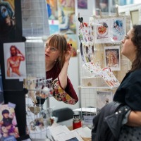 Künstlerstand mit Besucher:innen in der New Artist Alley auf der Manga-Comic-Con 2025 Künstlerstand mit Besucher:innen in der New Artist Alley auf der Manga-Comic-Con 2025