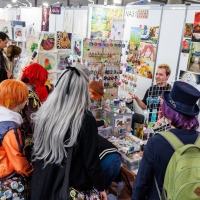 Künstlerstand mit Besucher:innen in der New Artist Alley auf der Manga-Comic-Con 2025 Künstlerstand mit Besucher:innen in der New Artist Alley auf der Manga-Comic-Con 2025