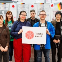 Gruppenfoto mit 6 Personen, die ein Schild mit dem Tancho Award Logo hochhalten auf der Manga-Comic-Con 2025 Gruppenfoto mit 6 Personen, die ein Schild mit dem Tancho Award Logo hochhalten auf der Manga-Comic-Con 2025